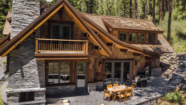 A two-story log cabin with a stone exterior, a balcony, and a patio area with outdoor furniture.