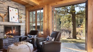 Ein gemütliches Zimmer mit Kamin, Ledersesseln, einem Schachbrett und einem großen Fenster mit Blick auf einen Wald.