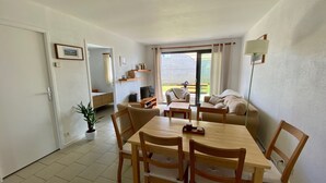 A dining area with a wooden table and chairs, a television, and a sofa in the background. - Small garden level for a seaside holiday (LE CONQUET)