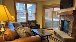 A living room with a leather sofa, a coffee table, a fireplace, and a TV mounted above it. - River Run - Steps to Ski, Hot Tubs, Heated Pool, Ice Rink (Keystone)
