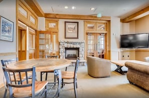 A hotel lobby with a stone fireplace, a round wooden table with chairs, a sofa, and a television mounted on the wall. - River Run - Steps to Ski, Hot Tubs, Heated Pool, Ice Rink (Keystone)