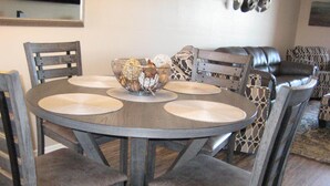 A round dining table with four chairs, a bowl with decorative items, and a patterned sofa in the background. - Vacation worthy Gilbert resort setting (Mesa)