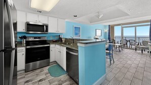 Una cocina moderna con electrodomésticos de acero inoxidable, un muro de acento azul y un balcón con mobiliario exterior.