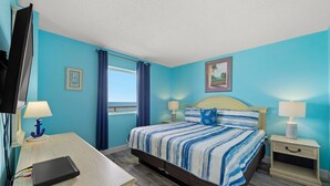 Una habitación con cama, escritorio, televisión y ventana con cortinas.