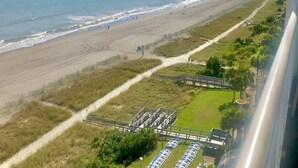 Vista de una playa con cielo despejado, arena, un sendero para caminar y un estacionamiento con coches.