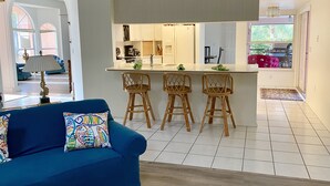 Ett modernt kök med en central köksö, barstolar och en matplats med en blå soffa och mönstrade kuddar.