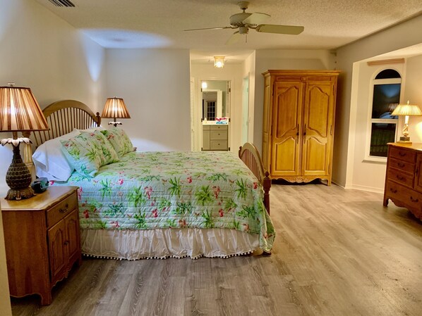 A bedroom with a bed, two bedside lamps, a wooden wardrobe, and a ceiling fan.