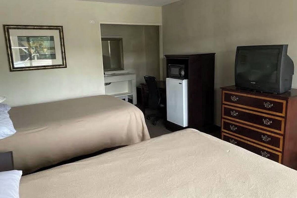 Une chambre d’hôtel avec deux lits, un bureau, une télévision et une commode.