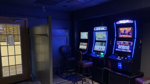 A room with wooden flooring, a door with a window, and three slot machines with illuminated screens.