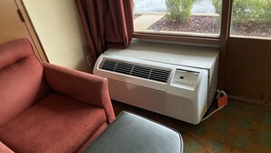 A room with a red armchair, a grey ottoman, and a white air conditioning unit.