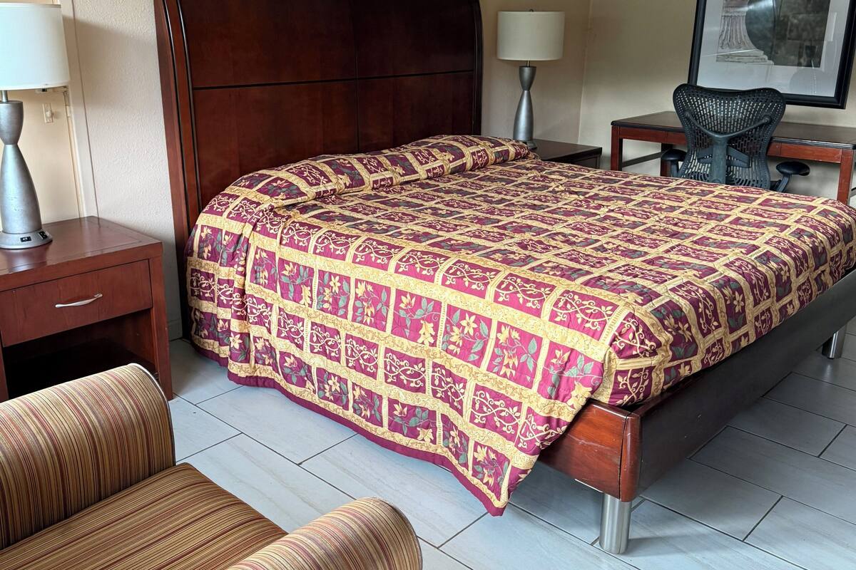 Une chambre d’hôtel avec un grand lit, deux tables de chevet avec des lampes, une chaise et un bureau avec une autre chaise.