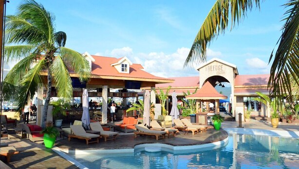 A resort pool area with lounge chairs, umbrellas, and a building labeled "REFUGE". - Sunset Beach View - Luxury Studio next to The Morgan Resort (Maho, Sint Maarten)