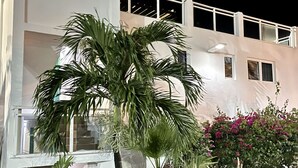 A multi-story building with balconies, a palm tree, and various shrubs. - Sunset Beach View - Luxury Studio next to The Morgan Resort (Maho, Sint Maarten)