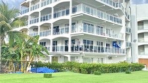 A multi-story hotel with balconies, a well-maintained lawn, and palm trees. - Sunset Beach View - Luxury Studio next to The Morgan Resort (Maho, Sint Maarten)