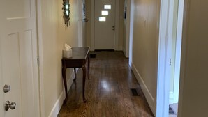 Um corredor com piso de madeira, paredes brancas e uma luminária no teto.
