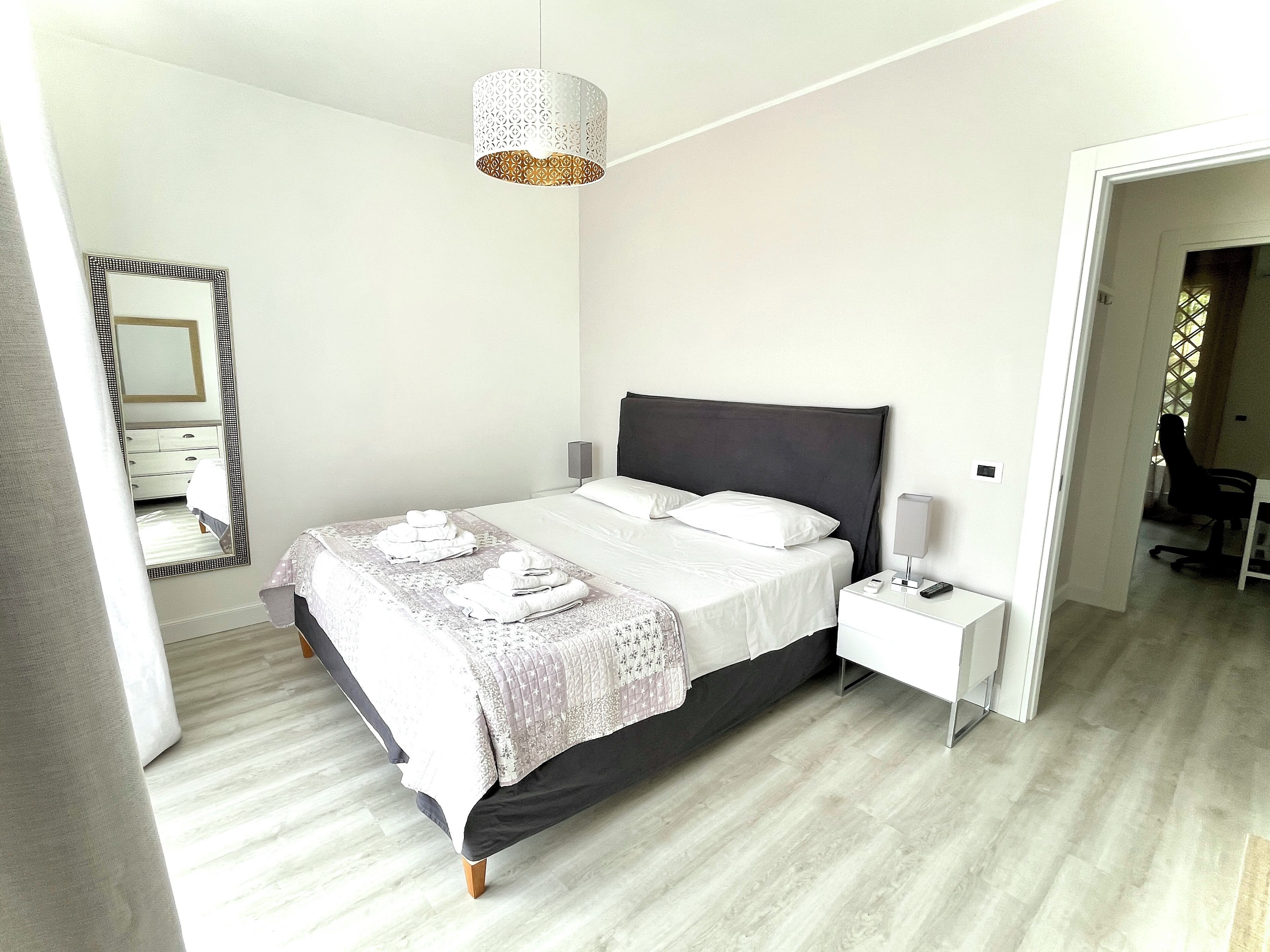 Un dormitorio moderno con una cama, mesitas de noche, un espejo y una lámpara colgante.