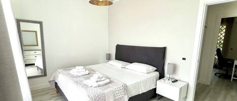 Un dormitorio moderno con una cama, mesitas de noche, un espejo y una lámpara colgante.