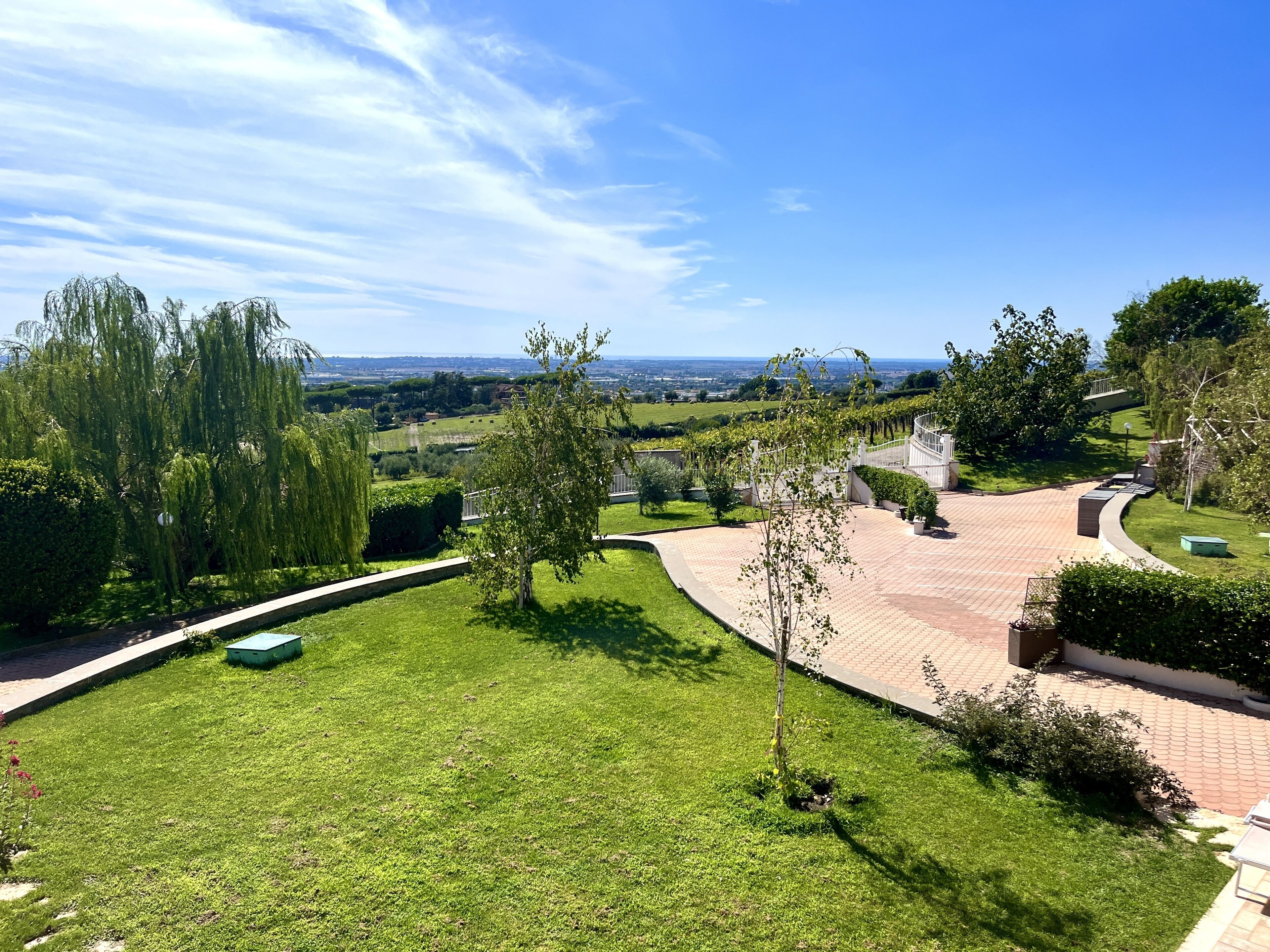 A landscaped garden with a curved pathway, a small pond, and a view of distant fields.