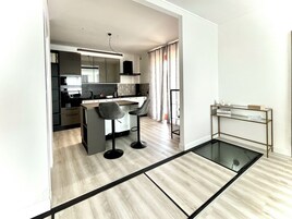 Una cocina moderna con una isla central, taburetes de bar y una mesa de vidrio.
