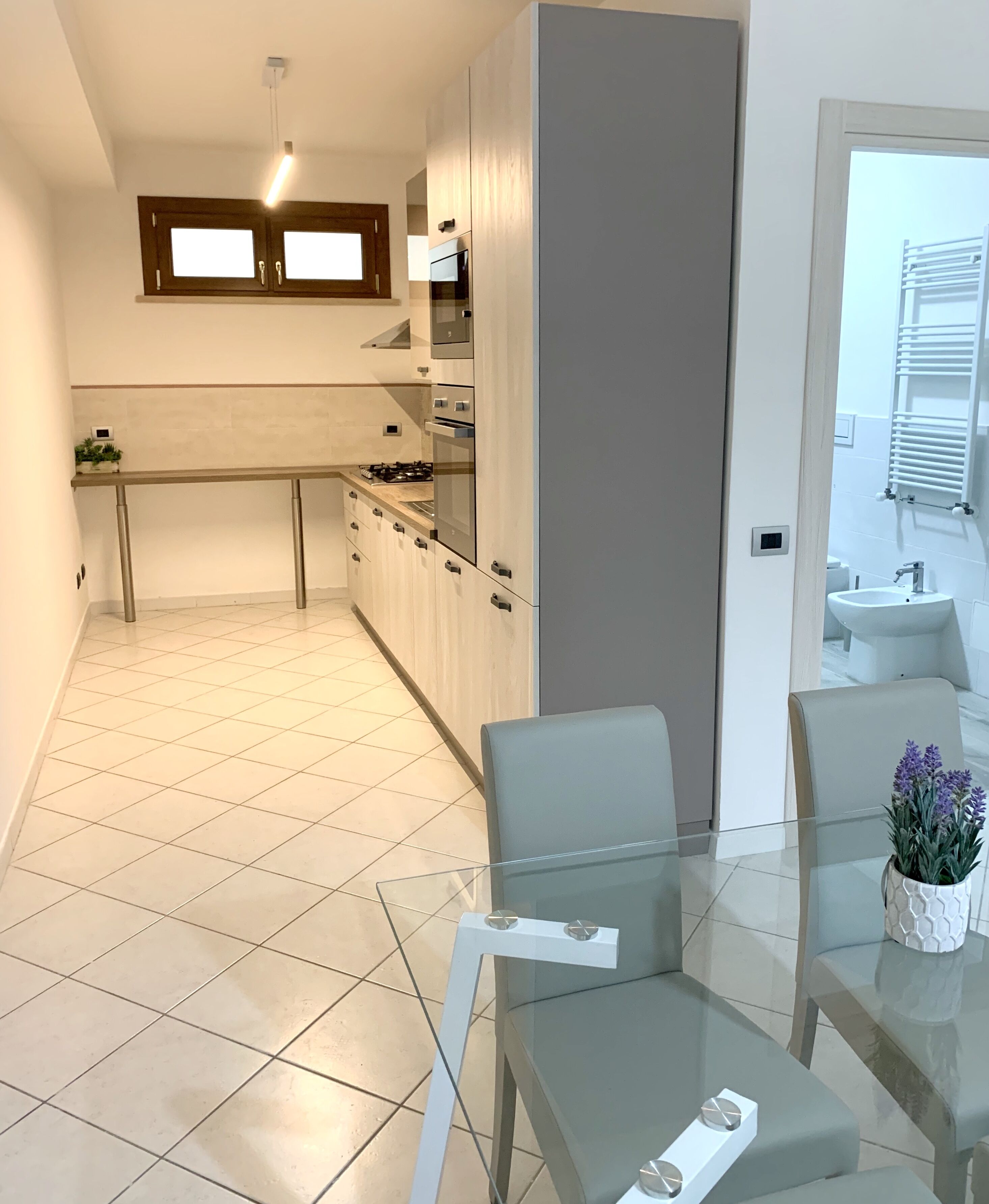 A modern kitchen with a central island, a dining area with a glass table, and a view of the living area.