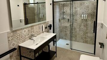 Une salle de bain moderne dotée d’un grand miroir, d’un lavabo double, d’une cabine de douche et de toilettes.