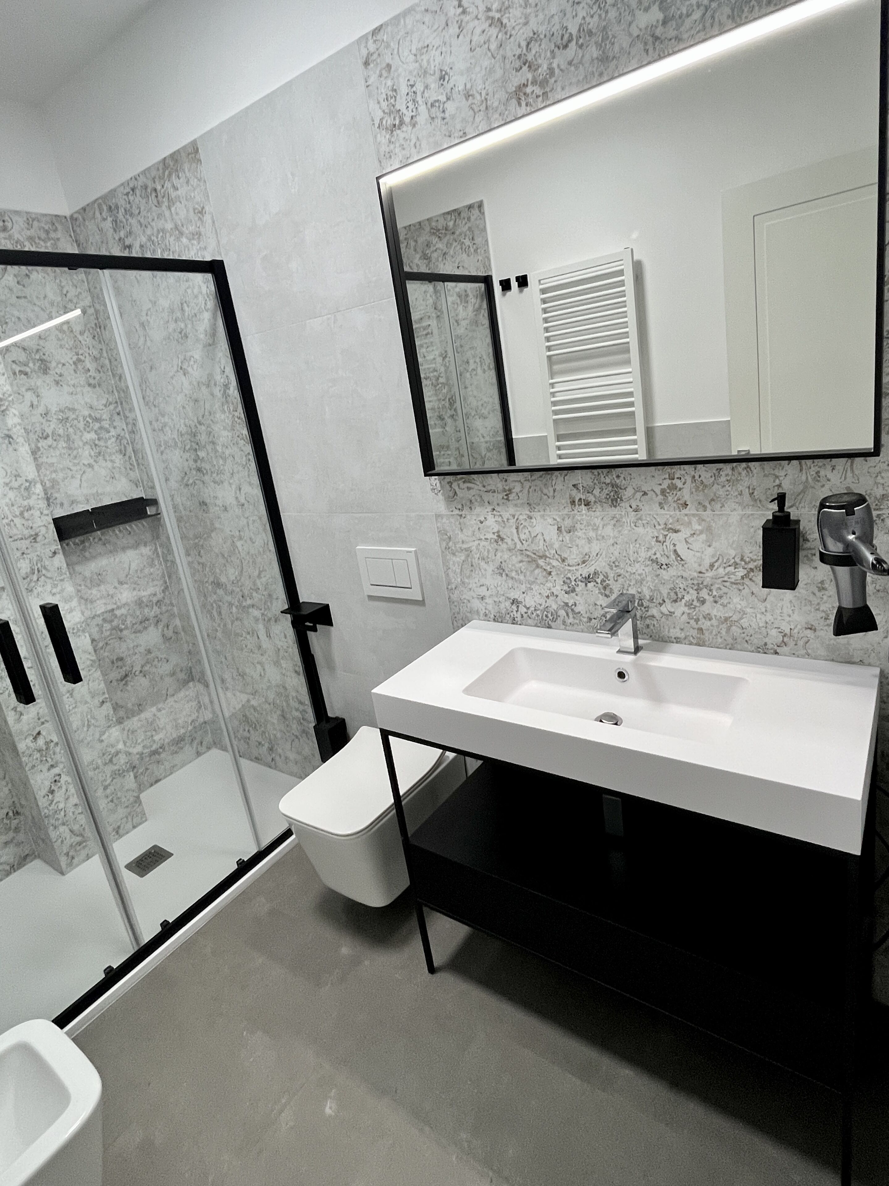 Une salle de bain moderne avec un lavabo blanc, une cabine de douche en verre et un mur décoré d’un motif marbré.