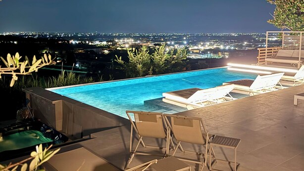 A rooftop pool with lounge chairs and a view of the city at night. - Cape House (Albano Laziale)