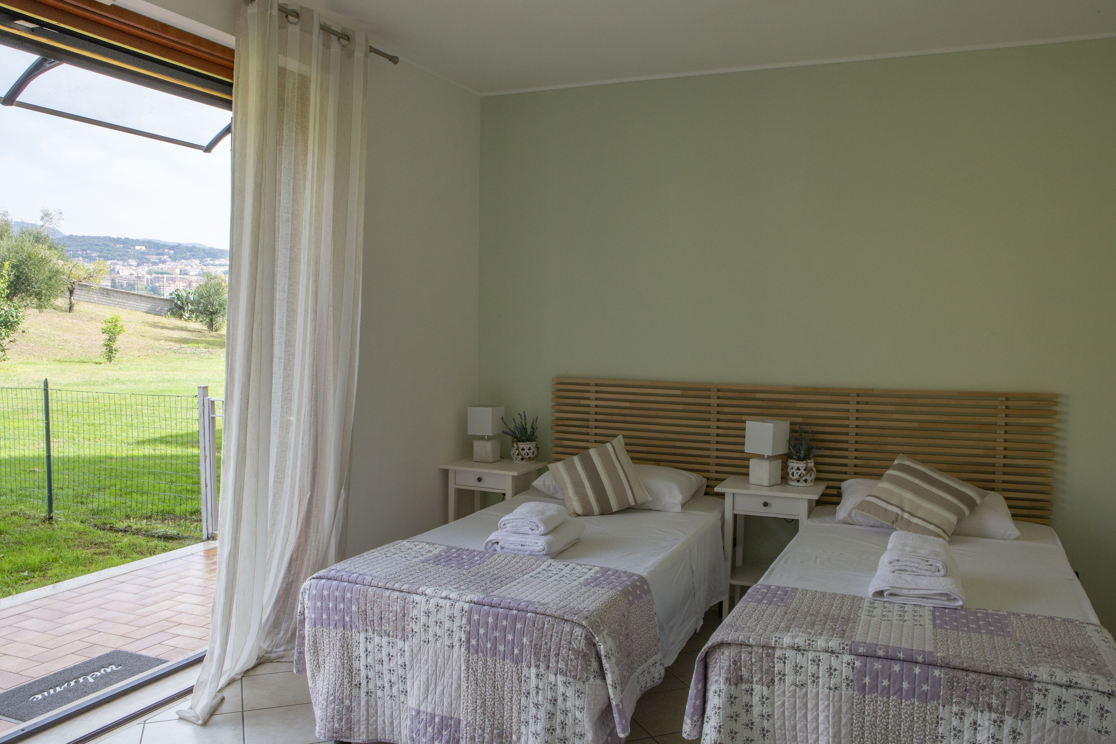 A bedroom with two beds, a view of the outdoors, and a window with curtains.