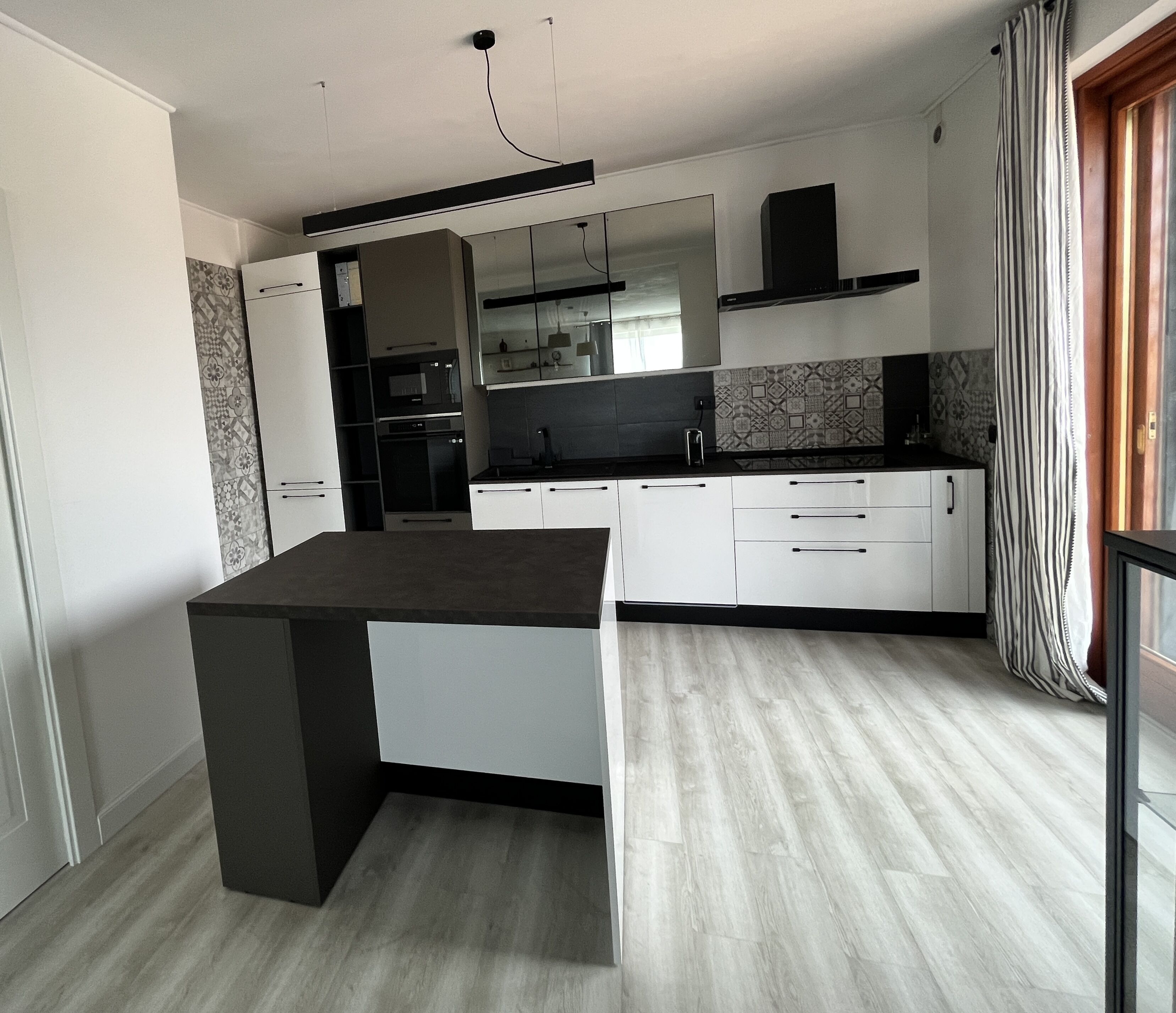 Una cocina moderna con armarios blancos, encimera negra y horno empotrado.