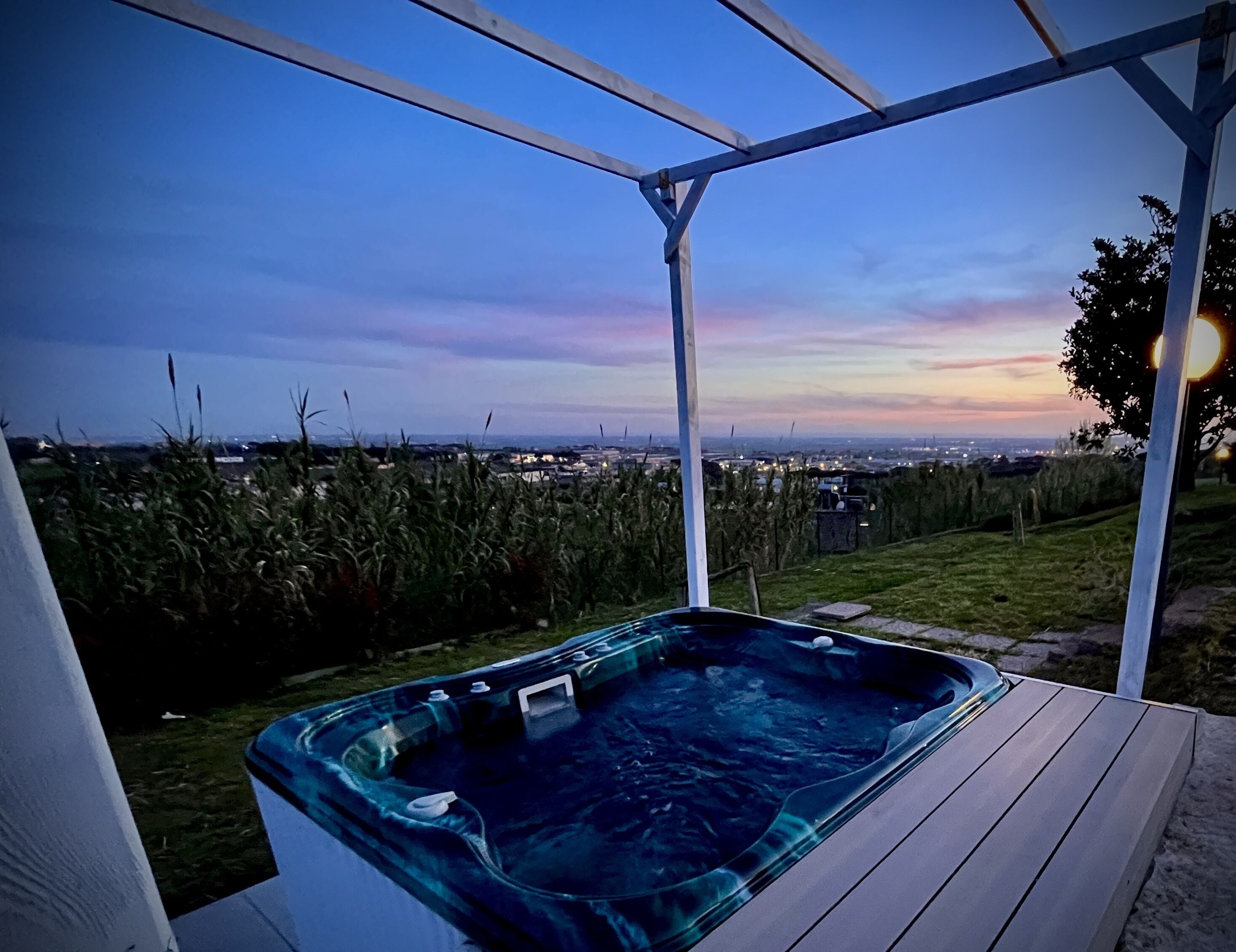 A hot tub under a pergola with a cityscape view at dusk.
