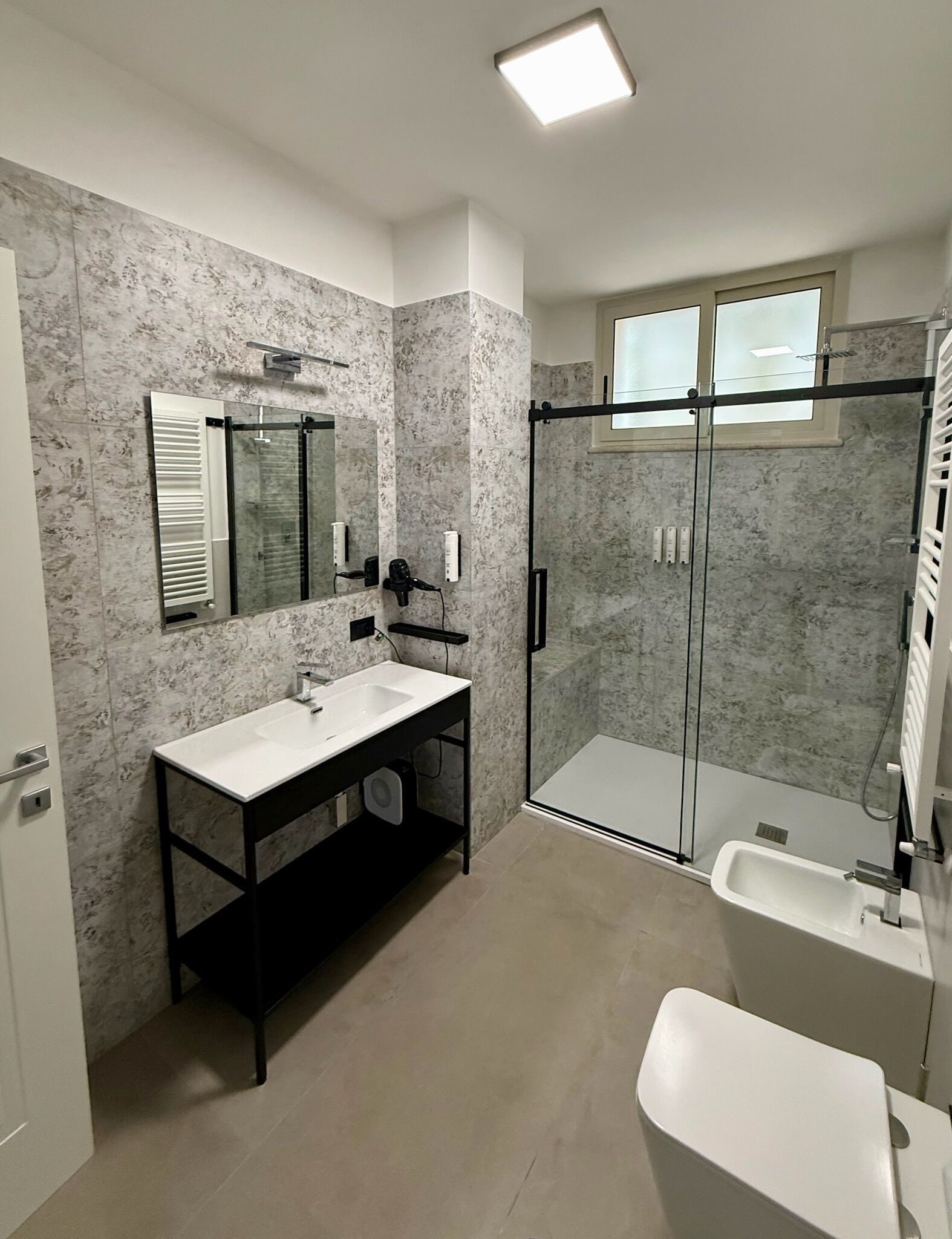 A modern bathroom with a marble backsplash, a large mirror, a vanity with a sink, a glass shower enclosure, and a toilet.
