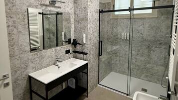 A modern bathroom with a marble backsplash, a large mirror, a vanity with a sink, a glass shower enclosure, and a toilet.