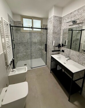 Een moderne badkamer met een douchecabine van glas, een witte wastafel en een grote spiegel.