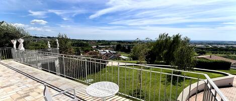 Een terras met een tafel en stoelen, uitzicht op een groen landschap en een heldere lucht.