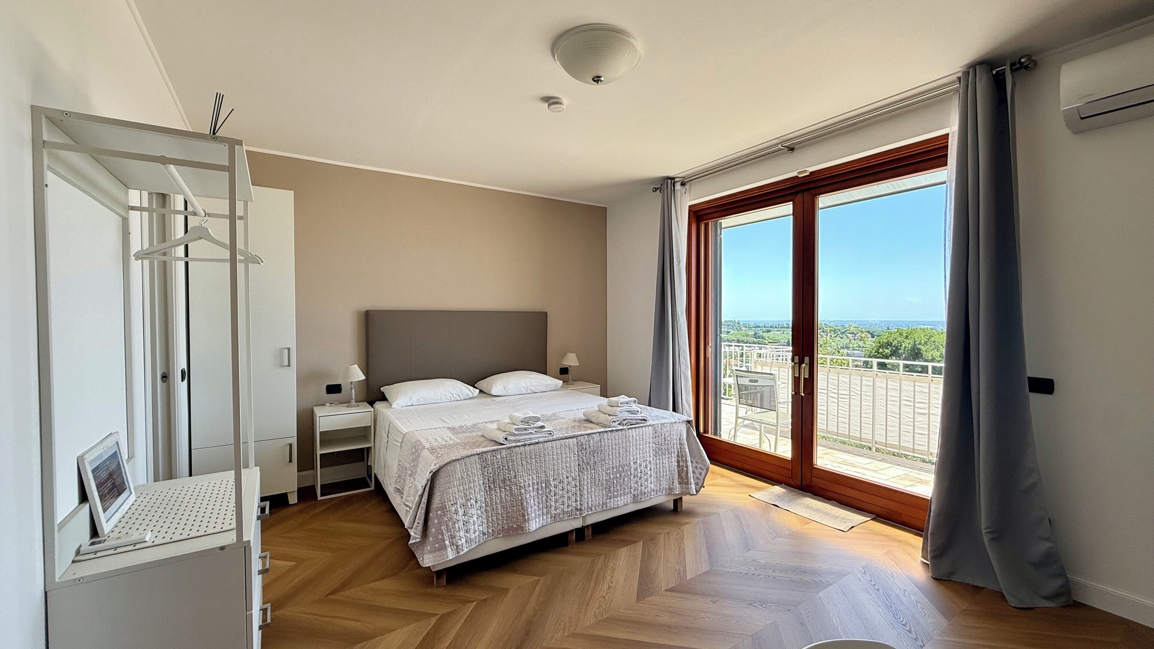 A bedroom with a bed, bedside tables, a wardrobe, a view through a sliding glass door, and a ceiling light.