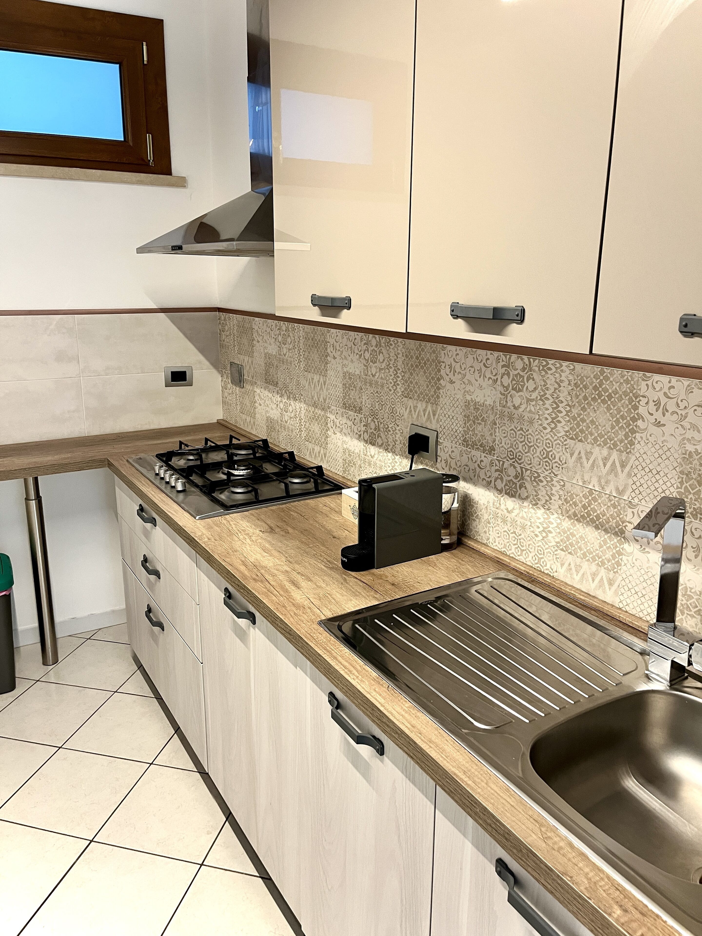 A modern kitchen with light wood cabinets, a gas stove, a toaster, and a stainless steel sink.