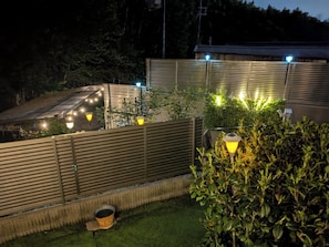 A rooftop garden with metal railings, potted plants, and outdoor lighting.