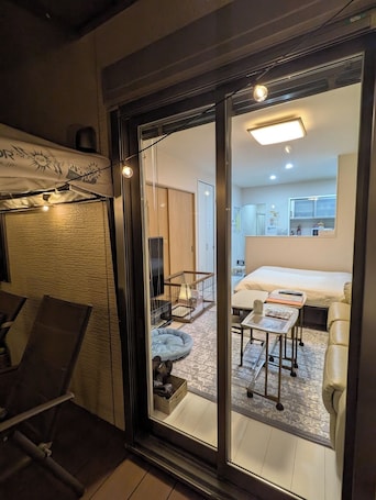 A modern hotel room with a glass door leading to a balcony, a bed, a small table, and a pet bed.