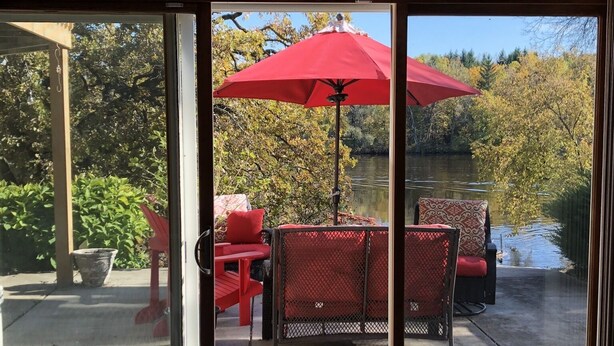 A room with a sliding glass door leading to an outdoor patio with red chairs and a red umbrella. - Rock River Haven - charming, spacious, peaceful (Watertown)