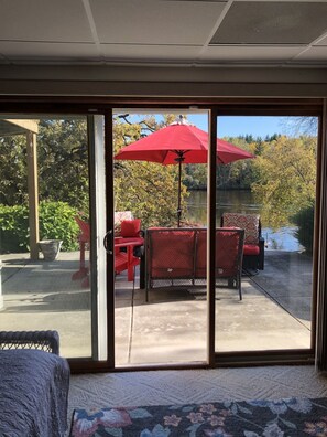 Een kamer met een schuifdeur die uitkomt op een terras buiten met rode stoelen en een rode parasol.