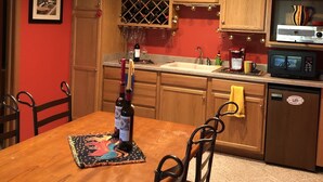 A compact kitchen with wooden cabinets, a dining table, and chairs. There is a wine bottle on the table. - Rock River Haven - charming, spacious, peaceful (Watertown)