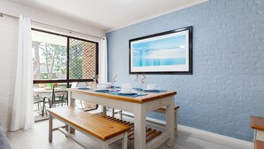 A dining area with a table set for four, a bench, and a framed picture on the wall. - Bay Parklands, 57/2 Gowrie Ave - ground floor unit with pool, tennis court & aircon (Nelson Bay)