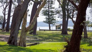 A park with a wooden bench, a small shelter, and a lake in the background. - Bay Parklands, 57/2 Gowrie Ave - ground floor unit with pool, tennis court & aircon (Nelson Bay)
