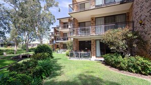 A multi-story residential building with balconies, a well-maintained lawn, and surrounding greenery. - Bay Parklands, 57/2 Gowrie Ave - ground floor unit with pool, tennis court & aircon (Nelson Bay)
