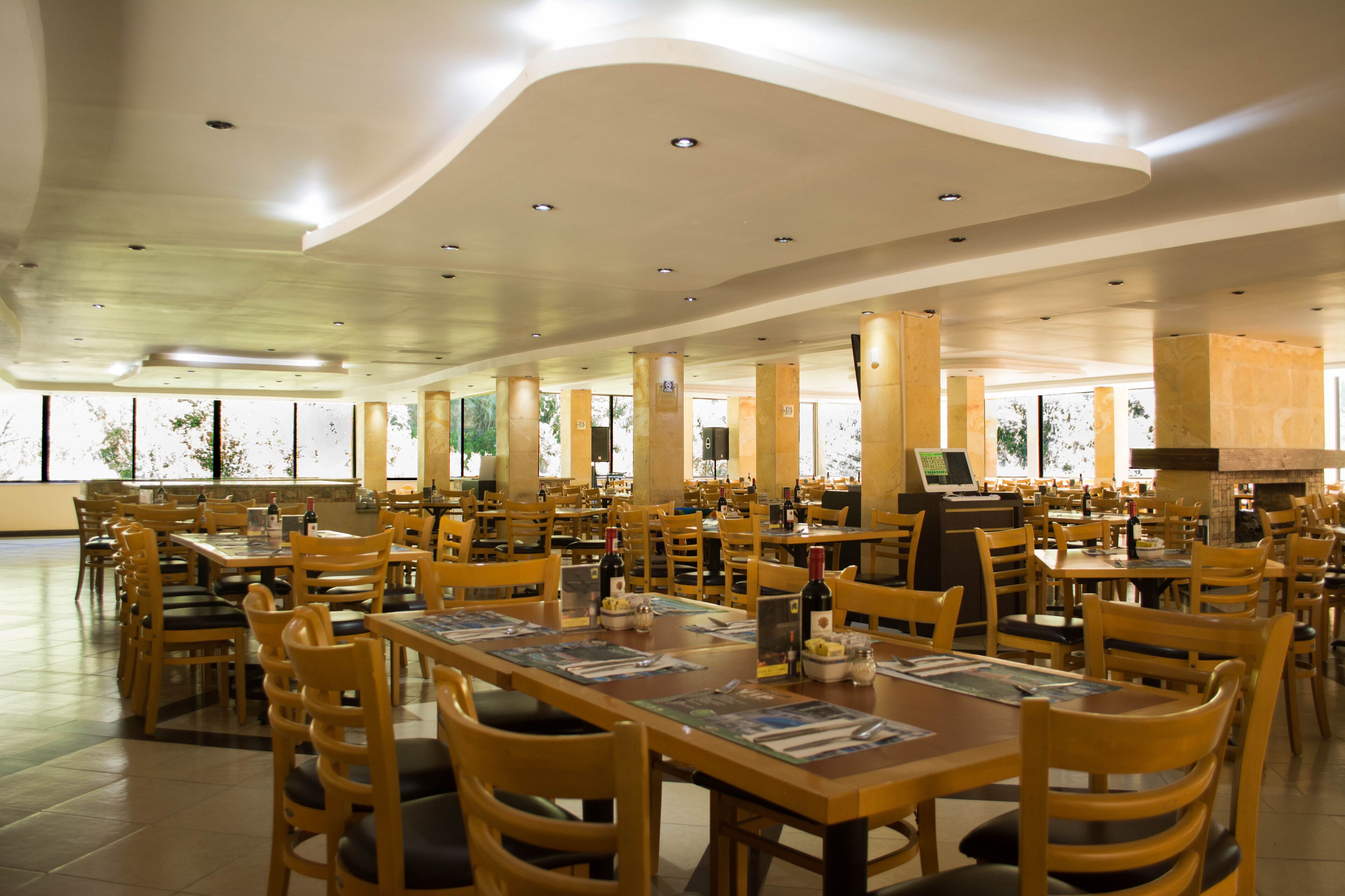 A spacious restaurant with multiple tables and chairs, large windows, and a high ceiling.