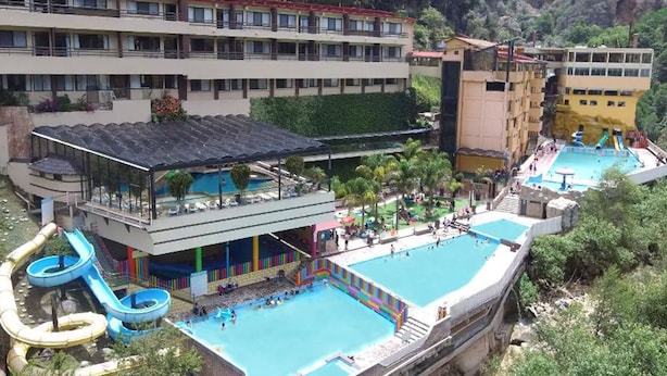 Un hotel con varias piscinas, un tobogán acuático y vistas a una zona montañosa.