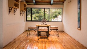 Una habitación con suelo de madera, una mesa redonda con cuatro sillas, un ventanal con vistas a zonas verdes y apliques decorativos en la pared.
