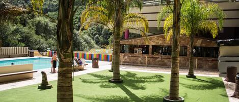 Uma área de piscina com palmeiras, um muro de pedra e um edifício com telhado inclinado.