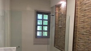 Un baño con cabina de ducha de vidrio, una ventana con persianas, un inodoro y un perchero para toallas.