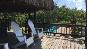 Una terraza de madera con mecedoras blancas y una estructura de techo de paja.